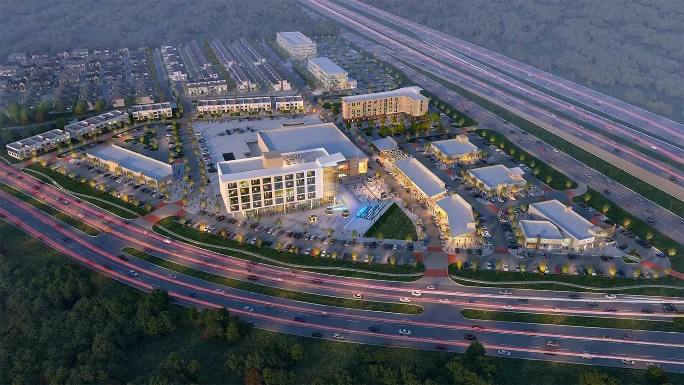 Aerial view at dusk of the West Plano district along State Highway 121, with the Interurban campus among low-rise buildings, surface parking and highway frontage